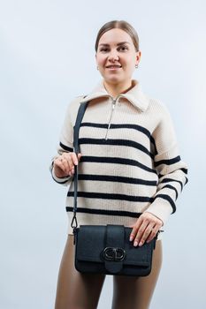 Beautiful young woman posing on a white background with a black handbag over her shoulder. A woman is holding a black leather shoulder bag. Women's fashion concept.