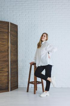 A young woman in black pants and a white shirt against a white brick wall, a stylish modern girl in white leather loafers