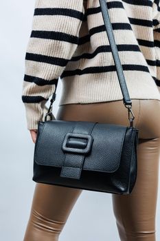 Beautiful young woman posing on a white background with a black handbag over her shoulder. A woman is holding a black leather shoulder bag. Women's fashion concept.