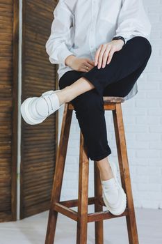 Legs of a young beautiful woman in black trousers and modern stylish white leather loafers. New collection of women's shoes spring-summer 2022