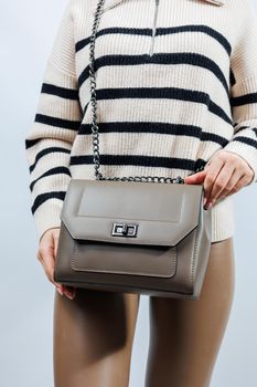 Small beige leather bag in a female hand on a white background. Shoulder bag. Woman with a beige handbag. Style, fashion, vintage and elegance.