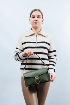 Small green leather bag in a female hand on a white background. Shoulder bag. A woman with a green handbag. Style, fashion, vintage and elegance.