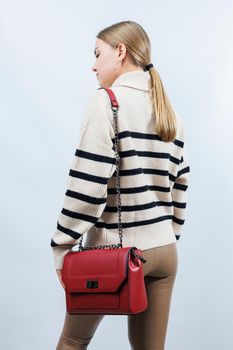 Small red leather bag in a female hand on a white background. Shoulder bag. Woman with a red handbag. Style, fashion, vintage and elegance.