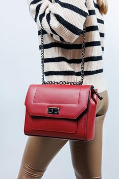 Small red leather bag in a female hand on a white background. Shoulder bag. Woman with a red handbag. Style, fashion, vintage and elegance.