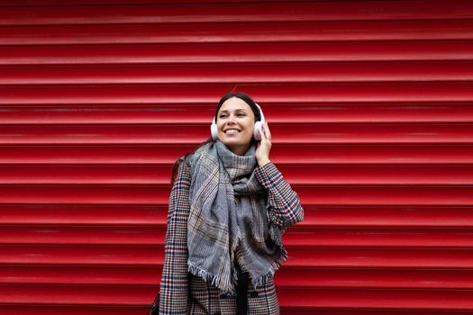 portrait of a cheerful young woman in headphones against the background of a relief red wall.