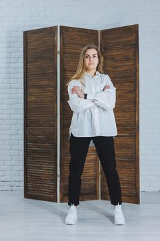 A beautiful stylish woman is wearing a white cotton shirt and black pants. Cheerful emotional girl in white sneakers