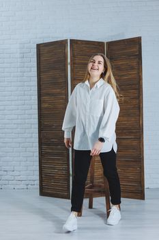 A beautiful stylish woman is wearing a white cotton shirt and black pants. Cheerful emotional girl in white sneakers