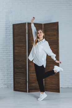 A beautiful stylish woman is wearing a white cotton shirt and black pants. Cheerful emotional girl in white sneakers