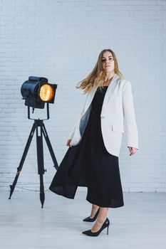 Attractive slender woman with long blond hair in a black dress and a beige jacket, long bare legs and high heels. Black pumps on female feet