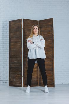 A beautiful stylish woman is wearing a white cotton shirt and black pants. Cheerful emotional girl in white sneakers