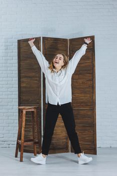 A beautiful stylish woman is wearing a white cotton shirt and black pants. Cheerful emotional girl in white sneakers