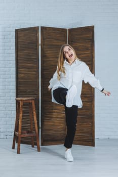 A beautiful stylish woman is wearing a white cotton shirt and black pants. Cheerful emotional girl in white sneakers