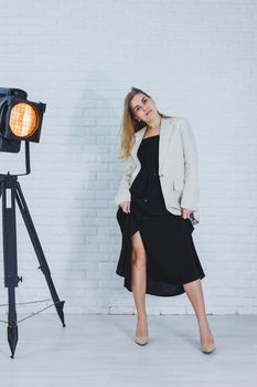 Beautiful young female legs in beige high-heeled shoes, a black long dress and a beige jacket. Open autumn and spring outfit with heeled shoes