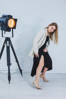 Beautiful young female legs in beige high-heeled shoes, a black long dress and a beige jacket. Open autumn and spring outfit with heeled shoes
