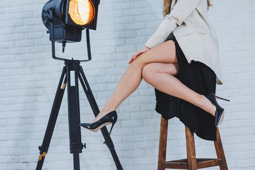 Close-up portrait of female legs in high heels. A lady in a black dress sits with long slender legs in black high-heeled shoes. Classic women's shoes