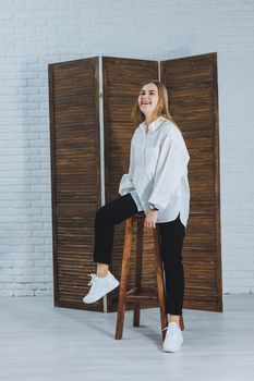 A beautiful stylish woman is wearing a white cotton shirt and black pants. Cheerful emotional girl in white sneakers