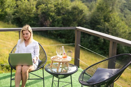 a woman with a laptop on a terrace in the mountains.