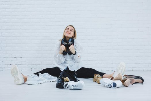 A woman sits on the floor in a dressing room between shoes and chooses new shoes for herself. Lady in a white shirt. Woman in white shoes.