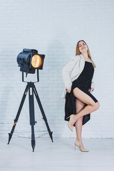 Beautiful young female legs in beige high-heeled shoes, a black long dress and a beige jacket. Open autumn and spring outfit with heeled shoes