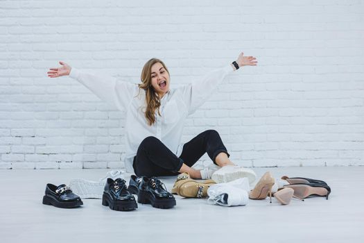 Stylish blonde choosing shoes while sitting on the floor. Side view of a lot of women's shoes on the floor, a choice of stylish shoes.