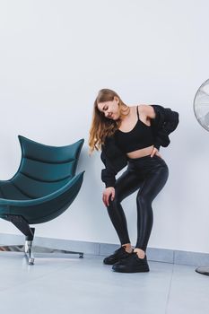 A stylish young woman she is dressed in black leather leggings, a top and a bomber jacket. The woman is wearing black leather lace-up sneakers.