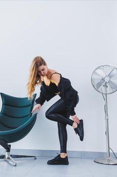 A stylish young woman she is dressed in black leather leggings, a top and a bomber jacket. The woman is wearing black leather lace-up sneakers.