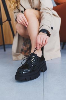 A young woman with slender beautiful legs in fashionable black leather shoes sits on a chair in the studio. Women's stylish loafers, close-up. Spring shoe collection