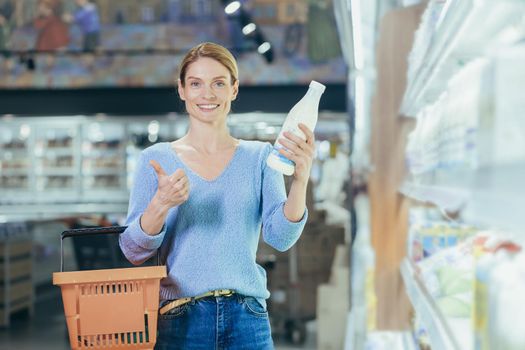 Portrait of a female buyer in a supermarket, a blonde housewife looking at the camera in the dairy department chooses milk and yogurt.