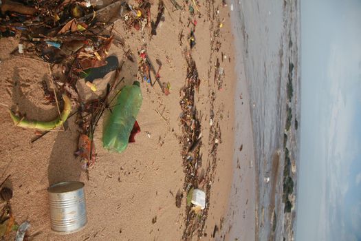 salvador, bahia, brazil - november 30, 2021: Plastic bottle and heaped garbage is seen in the sand of Costa Azul beach near the mouth of Rio Camurigipe in Salvador city.