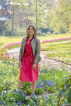 Happy young woman stands among the flower beds in the park and smiles with delight High quality photo