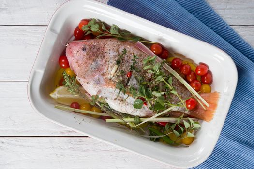 raw pink tilapia fish with vegetables in a baking dish, hands spice on the fish, step by step recipe for white wooden planks,High quality photo
