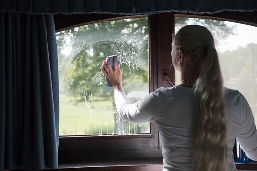 Woman cleaning window with special glass cleaner. Look through soapy window. High quality photo