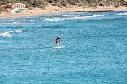 Man practicing paddle surfing through the deserted beaches of Ses Salines in the Ses Salinas National Park of Ibiza and Formentera, Spain.