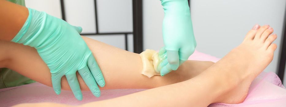 Waxing depilation procedure for removing hair on legs with sugaring paste in the beauty salon