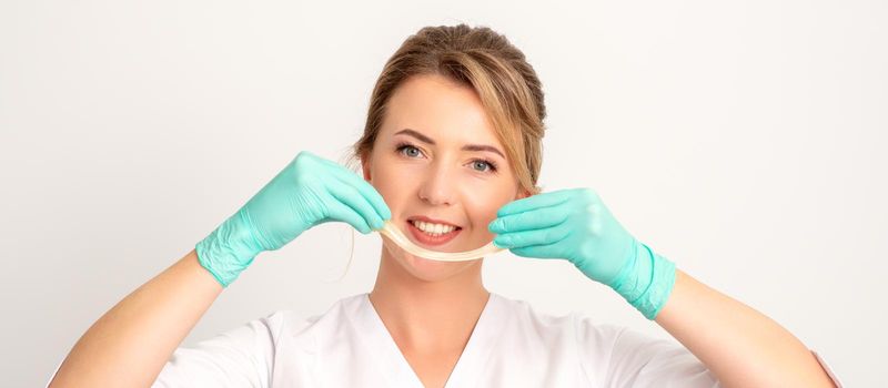 Young caucasian smiling female beautician holding wax for depilation over white background. Yellow sugar paste in hands master of depilation. Epilation concept