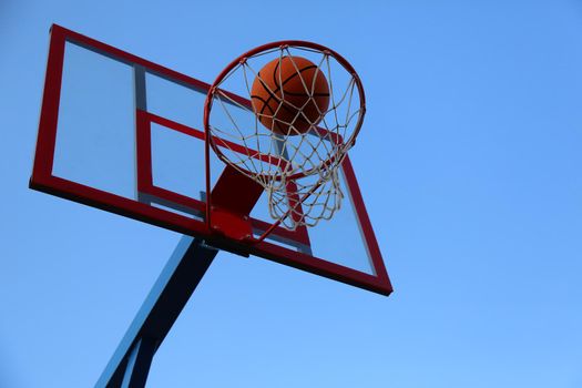 A basketball ball flies into a basket on a street basketball court. A basketball game. The ball against the sky in the goal.