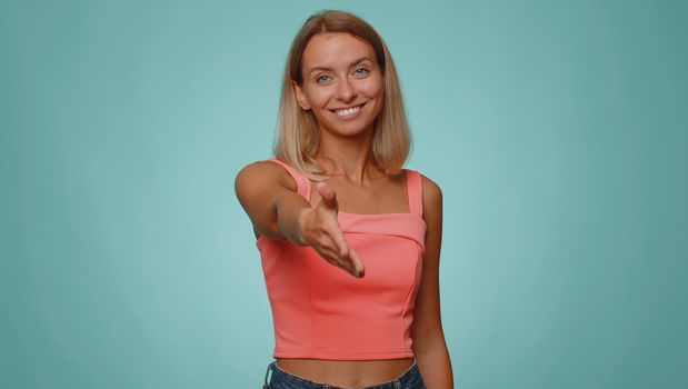 Friendly woman in crop top outstretching hand to camera, offering handshake, greeting with kind smile, welcoming showing solidarity, trust concept. Young adult girl isolated on blue studio background