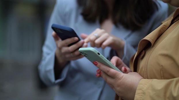 Close up focus on females hands using phones. Two women with smartphones on the street, the girl explains, shows, tells, demonstrates, gesticulates with her hand.