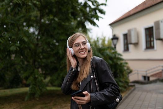 smiling young female student listening to music with headphones on the background of the urban landscape.