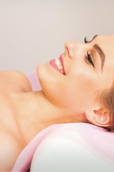 A beautiful smiling young woman is lying on a massage couch waiting for a massage in a massage room