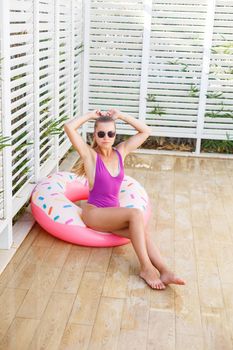 A young and attractive woman in sunglasses and a pink swimsuit. She holds an inflatable ring in her hands and smiles, summer vacation