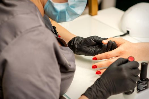 Professional manicure. A manicurist is painting the female nails of a client with red nail polish in a beauty salon, close up. Beauty industry concept