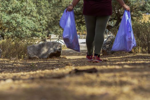 woman ecologist with garbage bags picking up garbage from the field and taking care of the environment