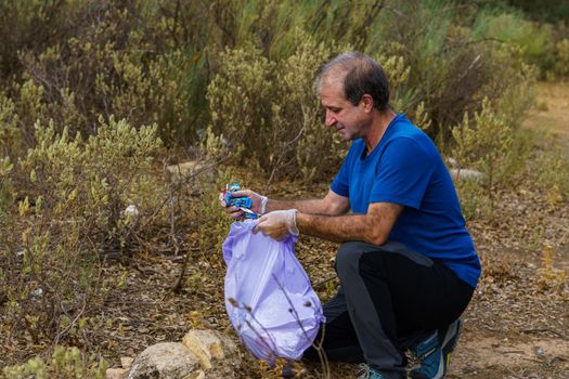 environmentalist man with garbage bags picking up garbage from the field and taking care of the environment