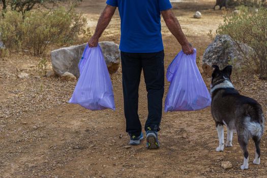 environmentalist man with garbage bags picking up garbage from the field and taking care of the environment