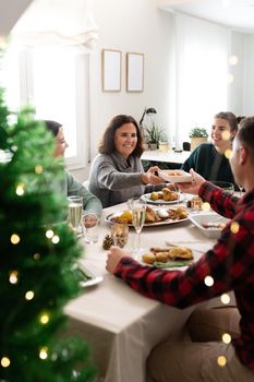 Mature caucasian woman pass plate of food to young man during family Christmas dinner. Vertical image. Holiday concept.