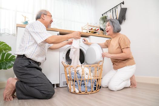 Senior couple working together to complete their household chores at the washing machine in a happy and contented manner. Husband and wife doing the usual tasks in the house.