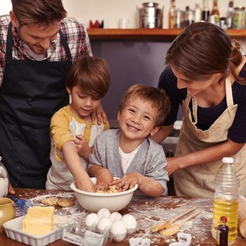 This is going to be delicious. Two cute little boys baking with their parents in the kitchen