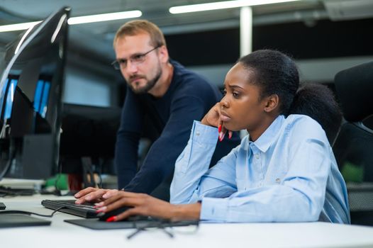 Colleagues look at the monitor and decide working moments. Caucasian man helps sad african woman solve computer problem