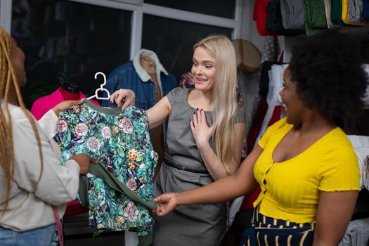 Two dark-skinned shopkeepers show a blouse to a new customer and tell her that this blouse is perfect just for her. A store and a tailor's store.